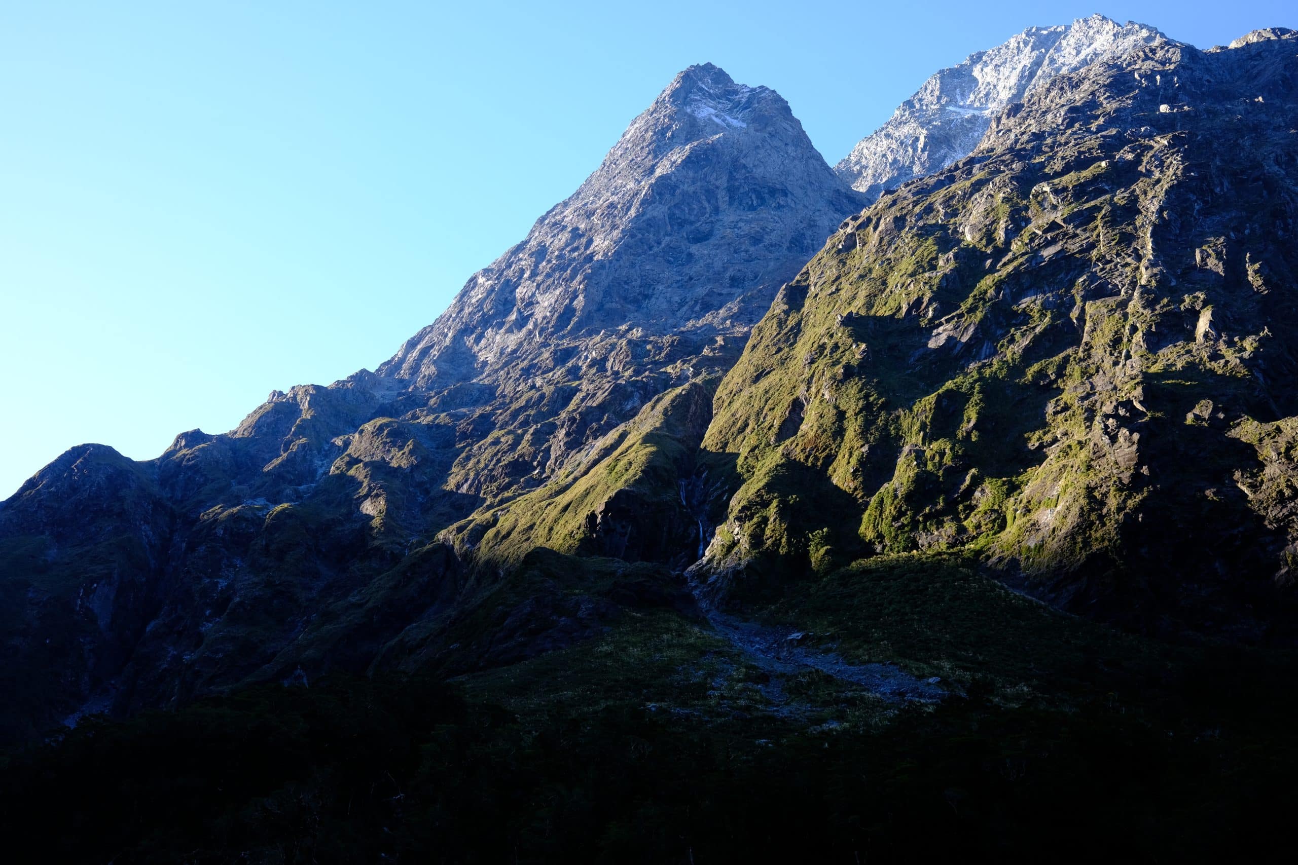 Sunlit alpine mountain peak rising above deep shadowed valleys in New Zealand, reflecting Neuromystics themes of inner transformation, elevation, and nature-guided healing.